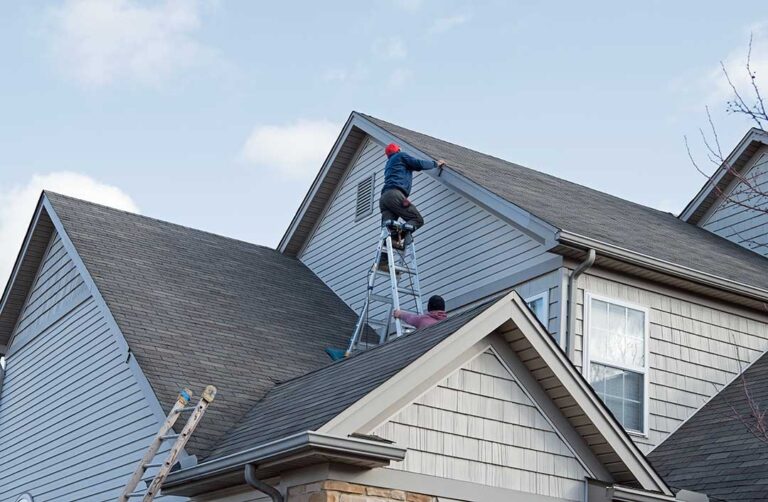 A person carefully cleaning gutters on a residential roof with a ladder and work gloves.