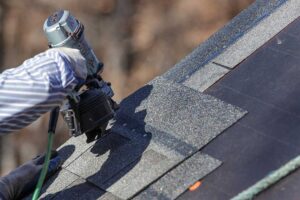 A person examines shingles and takes notes on a ladder during a residential roof inspection.