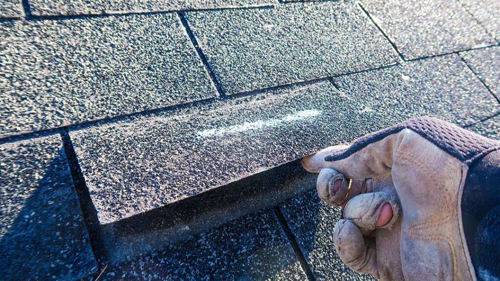 A person cleaning leaf debris from a house gutter with gloves and a small trowel.