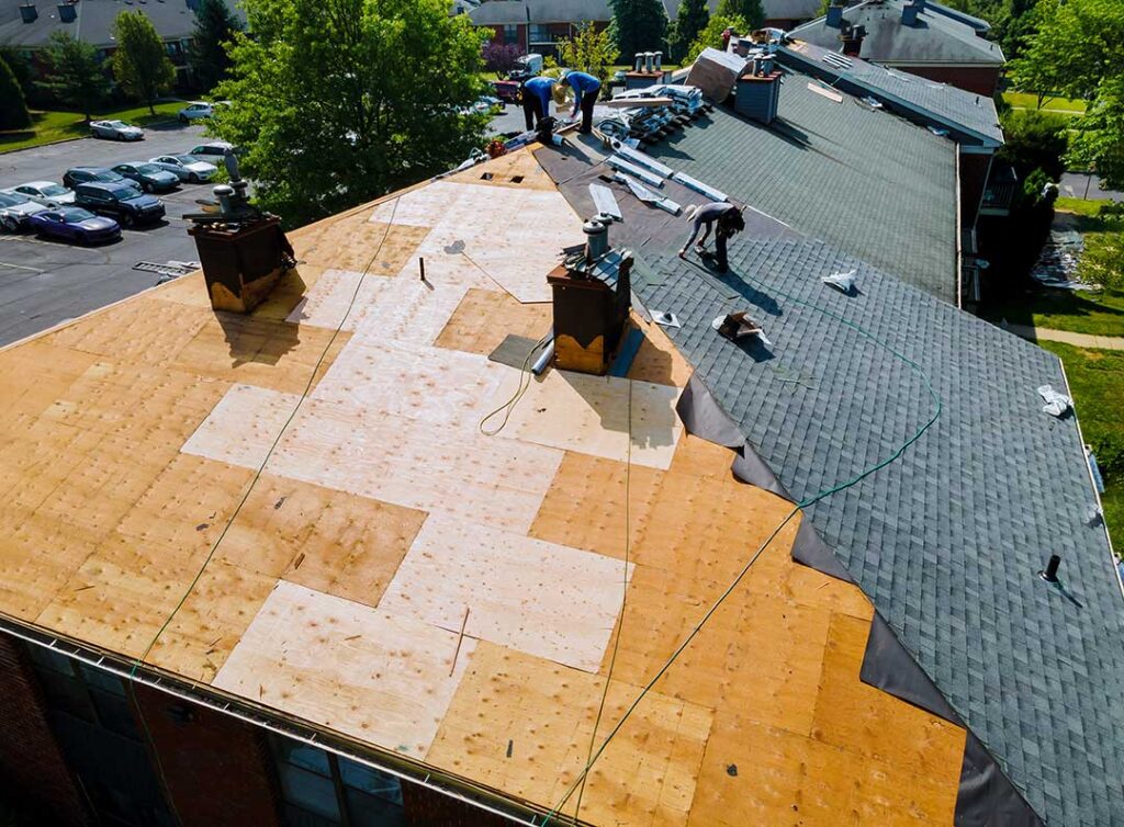 Person measuring the slope of a residential roof with a level and tape measure on a sunny day.