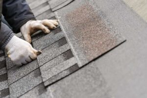 Person inspecting roof gutters from a ladder beside a home with leaves and autumn debris nearby.