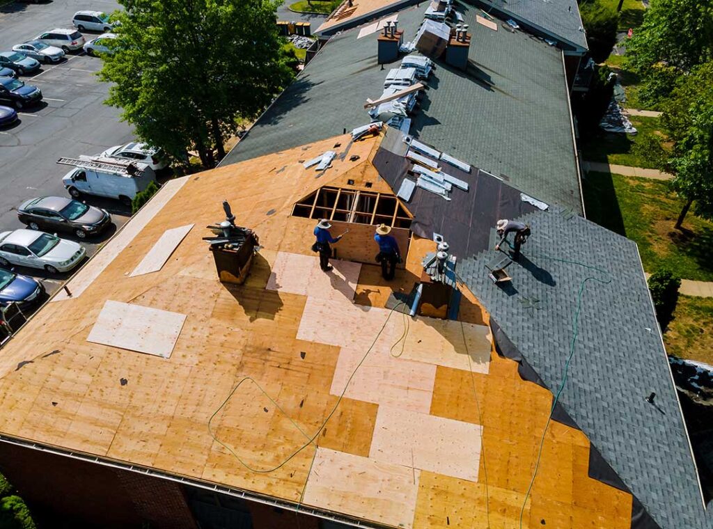 A homeowner examines damaged shingles and loose flashing beside a leaking roof section.