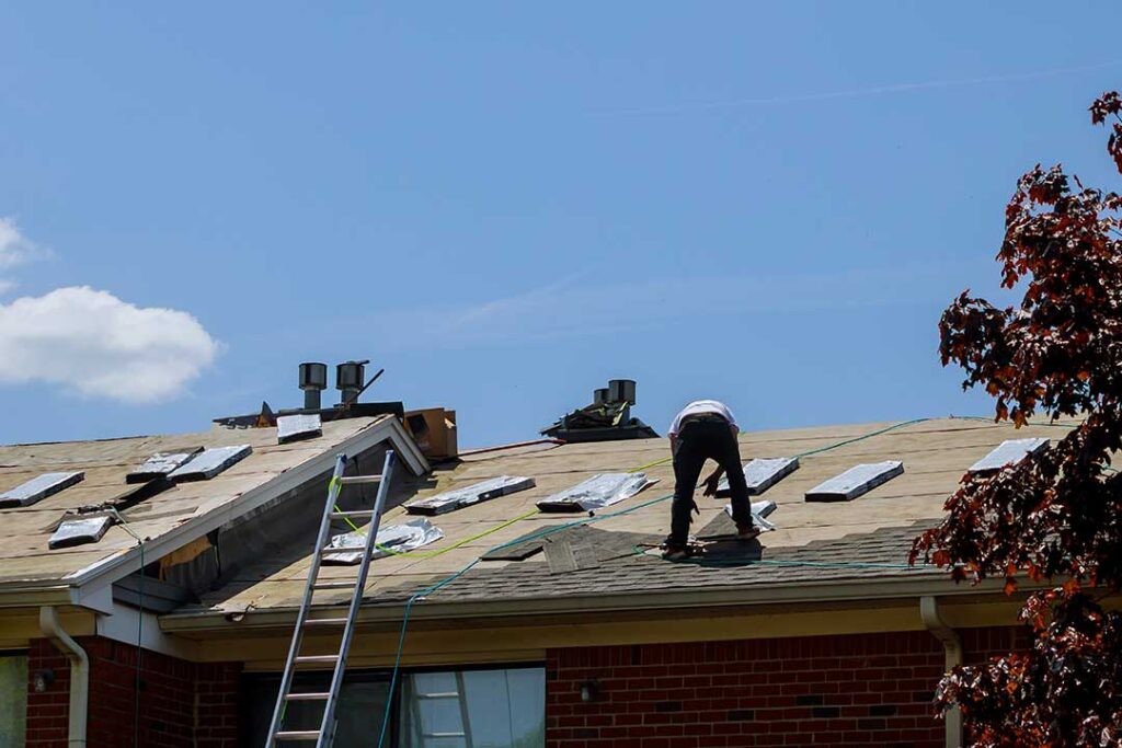 Workers use protective coverings and a secured ladder while renovating a house roof.
