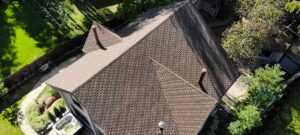 A peaked roof cricket rises behind a brick chimney with metal flashing directing water along both sides.