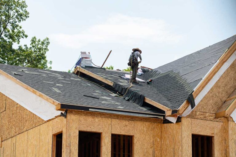 A homeowner examines damaged shingles and exposed flashing along a roof valley from a safe ladder position.