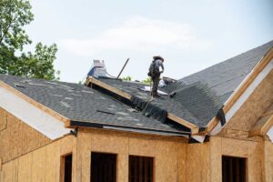 A homeowner examines roof shingles and attic moisture signs beside a residential roof.