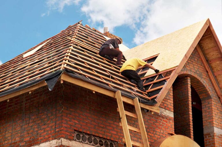 A homeowner examines a ceiling water stain beneath a roof leak while a bucket catches dripping water.